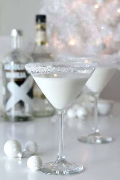 two martini glasses filled with white liquid on a table next to bottles and christmas decorations