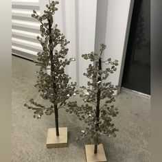 two small metal trees on wooden bases in front of a white wall and grey concrete floor