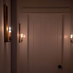 three candles are lit on the wall in front of a white door with two black knobs