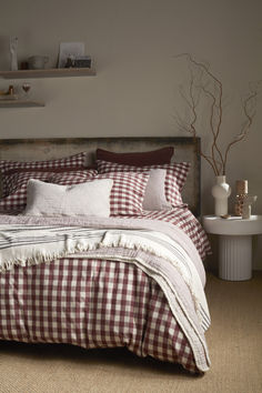 A cozy bed styled with burgundy gingham bedding, layered with textured neutral cushions and a striped throw. The room features earthy decor accents, including dried branches and a rustic headboard, creating a warm, autumnal, and rustic bedroom look. Duck Egg Bedding, Teal Bedding, Baby Cot Bedding, Wool Bed, Cosy Bed, 100 Cotton Duvet Covers, Yellow Bedding, Organic Cotton Bedding, Linen Store