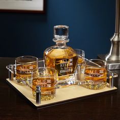 a wooden tray topped with glasses and a bottle of whiskey on top of a table