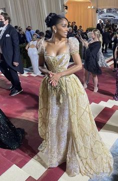 a woman in a gown standing on a red carpet with other people around the room