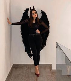 a woman in black is posing with wings on her head and hands behind her back