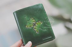 a hand holding a green leather wallet with four leaf designs on the front and side