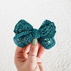 a hand holding a green crocheted bow on top of a white wall in front of the camera