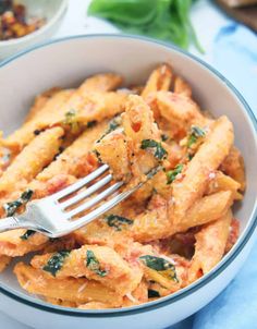 a bowl filled with pasta and spinach on top of a blue cloth next to a fork