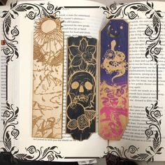 an open book with three different colored booksmarks on it's pages and one is decorated in gold, silver, and black