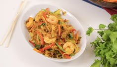 a white bowl filled with shrimp and veggies next to some chopsticks