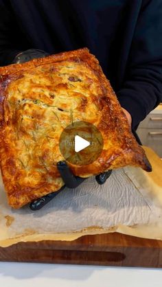 a person holding a square pizza on top of a wooden cutting board