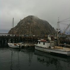 two boats in the water next to a large rock on a cloudy day with mountains in the background