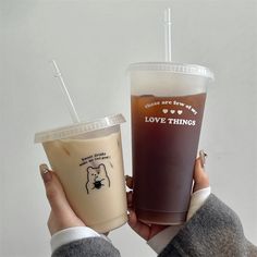 two people holding up cups with drinks in them, one is brown and the other is white