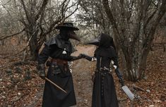 two people dressed in black standing next to each other on a path surrounded by trees