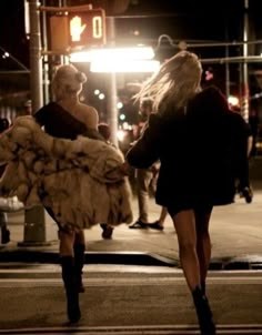 two women walking down the street at night with fur coats over their shoulders and legs