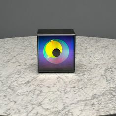 a square object sitting on top of a white marble table next to a gray wall