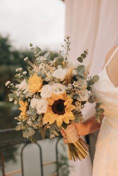 a bride holding a bouquet of sunflowers and greenery