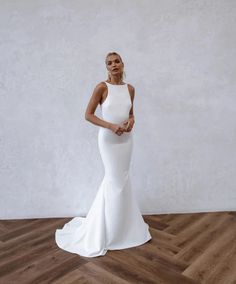 a woman in a white dress standing on a wooden floor with her hands behind her back