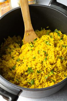 a pot filled with yellow rice next to a wooden spoon