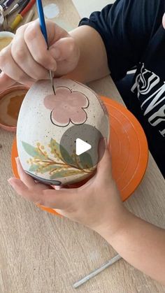 a person is painting a vase on an orange plate