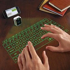 a person using a wireless keyboard on a wooden table with other electronic devices and books