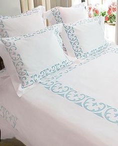 a bed with white sheets and blue trimmings in a room next to a window