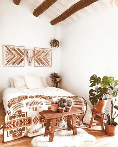 a bedroom with white walls and wooden flooring, potted plants on either side of the bed