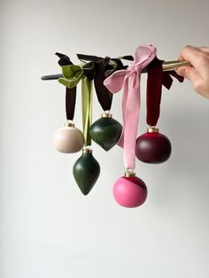 three ornaments hanging from a pink ribbon with green and red baubles attached to them