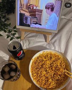 a bowl of noodles with chopsticks in front of a television set and drinks