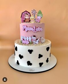 a pink and white cake with black polka dots on the bottom, topped with an assortment of small figurines