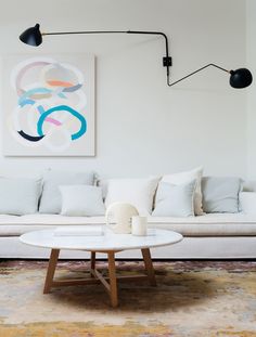 a living room with white couches and art hanging on the wall above it's coffee table