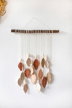 a white wall hanging with brown and beige leaves on it's side next to a clock