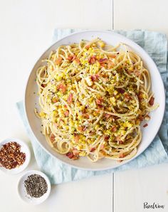 a white plate topped with pasta and sauce next to two small bowls filled with seasoning