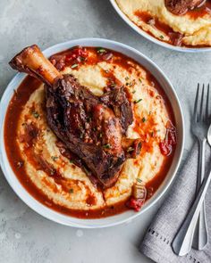 two plates of mashed potatoes with meat and sauce on them, next to silverware