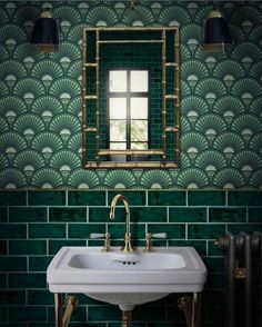 a white sink sitting under a mirror next to a green tiled wall with gold fixtures