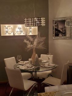 a dining room table with white chairs and lights on the wall above it that says eat