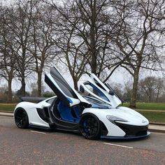 a white and blue sports car parked on the side of the road with its doors open