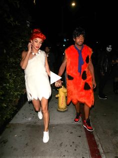 two people in costumes walking down a sidewalk