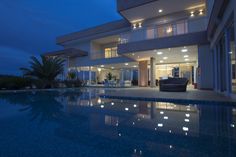 a large house with a swimming pool in front of it at night, lit up by lights on the windows