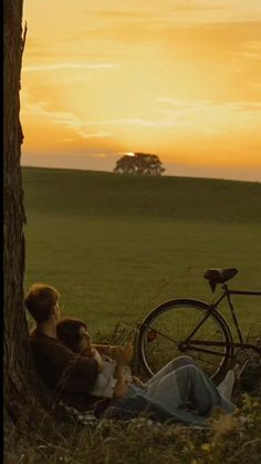 two people sitting under a tree with a bike in the background at sunset or dawn