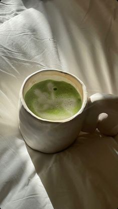 a white cup filled with green liquid on top of a bed