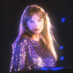 a woman with long hair wearing a purple sequin top and looking at the camera