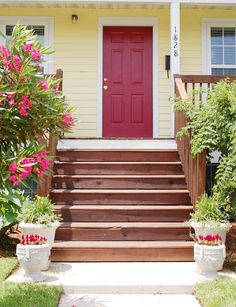 a red door sits on the front steps of a yellow house with potted flowers