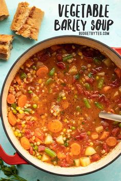 a red pot filled with vegetable soup next to crackers and parsley on a blue surface