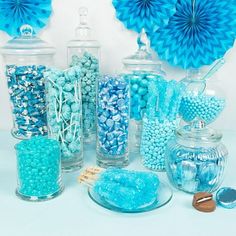 there are many candy in the glass vases and on the table is paper fans