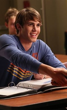 a young man sitting at a desk shaking hands with another person