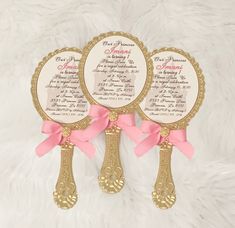 three golden spoons with pink bows are on a white furnishing area,