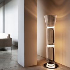 a tall glass vase sitting on top of a floor next to a white chair and wall