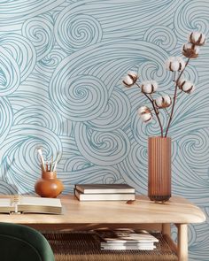 a wooden table topped with books and a vase filled with flowers next to a wall