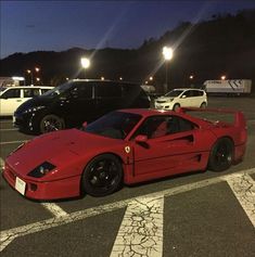 a red sports car is parked in a parking lot at night with other cars behind it