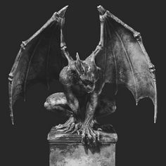 a statue of a gargoyle sitting on top of a stone block with its wings spread