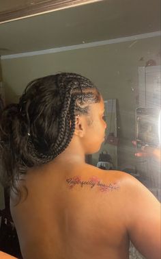 the back of a woman's head with braids in her hair and tattoos on her upper half